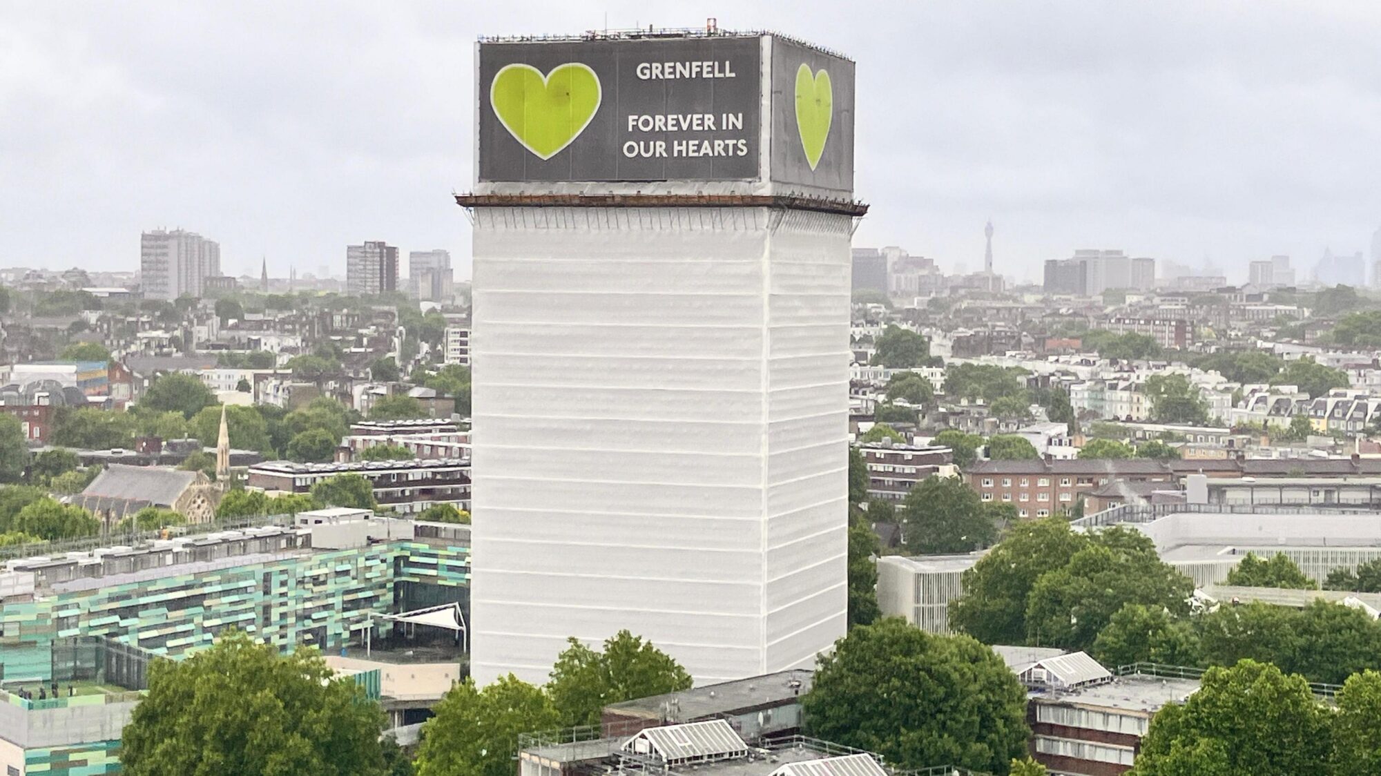 Grenfell Tower covered with tarp and a banner that reads: Grenfell- Forever in our Hearts
